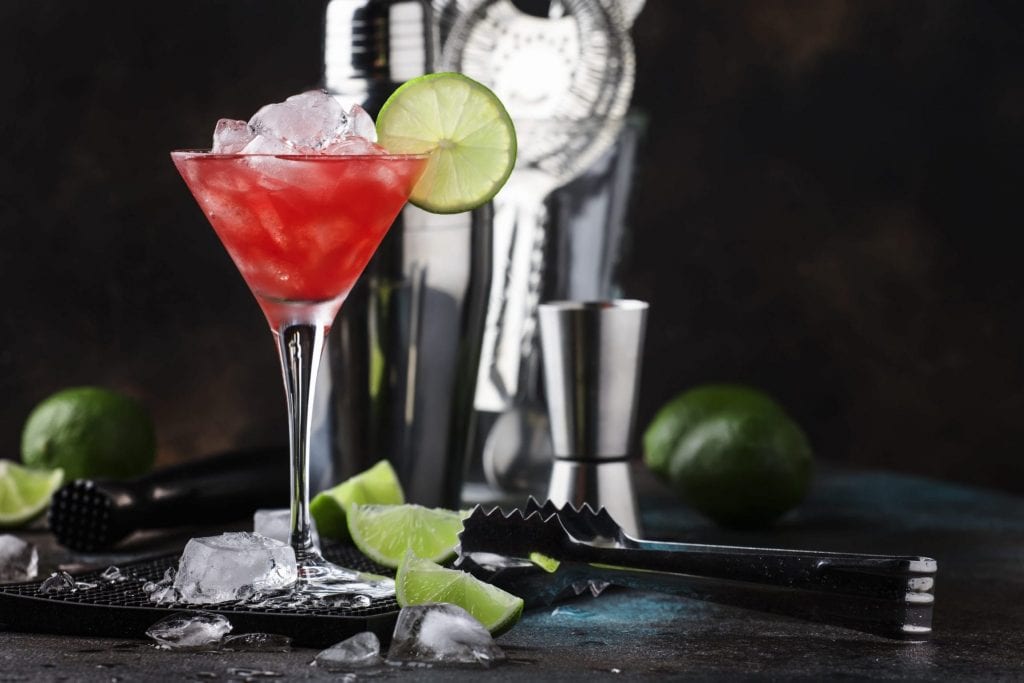 Red Watermelon alcoholic cocktail with vodka, juice, lime and crushed ice, metal bar tools, dark background